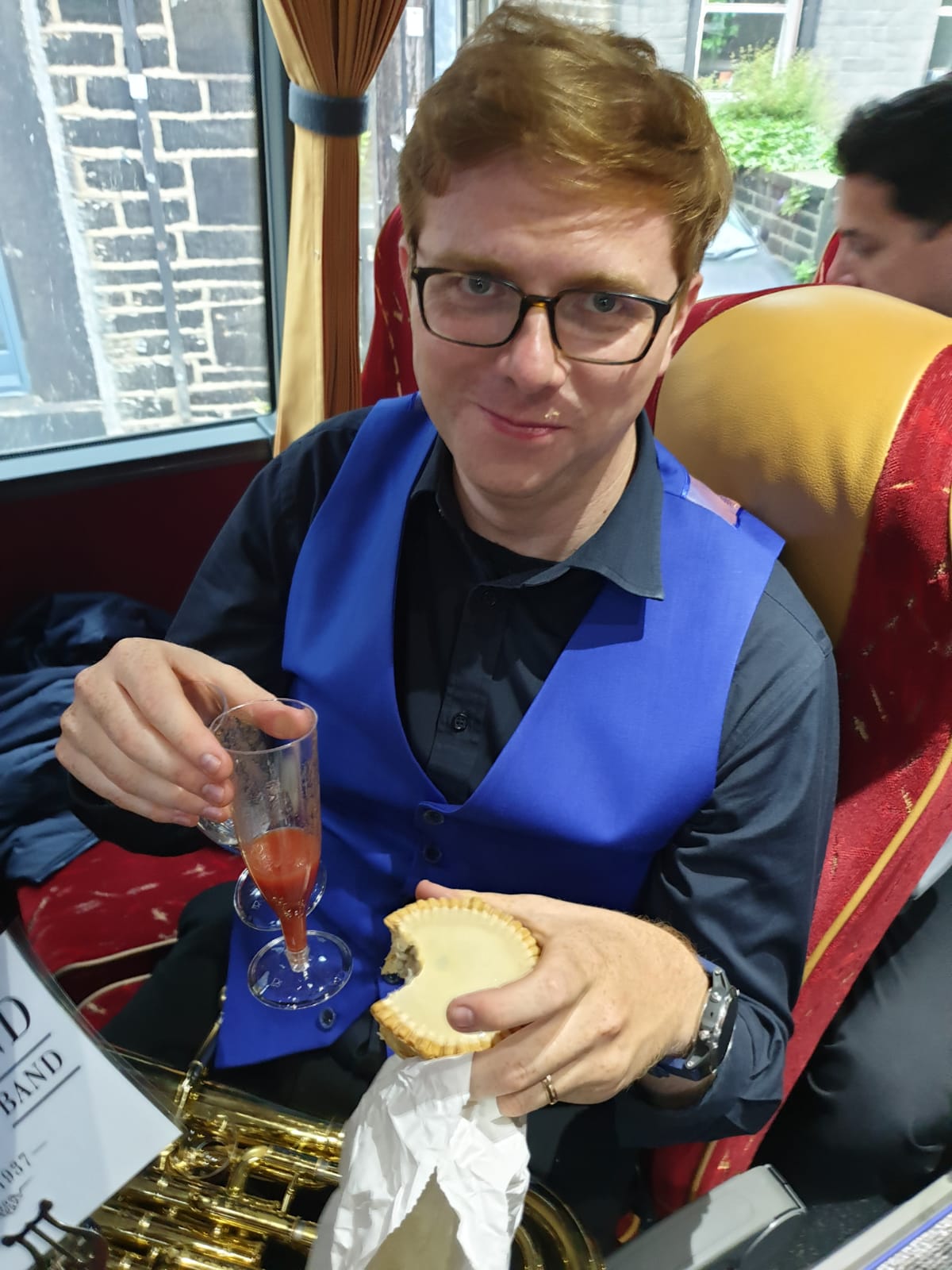 A player on the coach holding a champagne flute and a pork pie